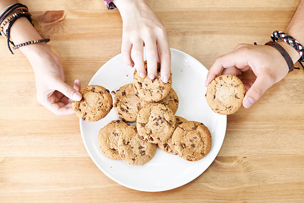 Sharing cookies Three hands taking cookies from a plate chocolate chip cookie top view stock pictures, royalty-free photos & images