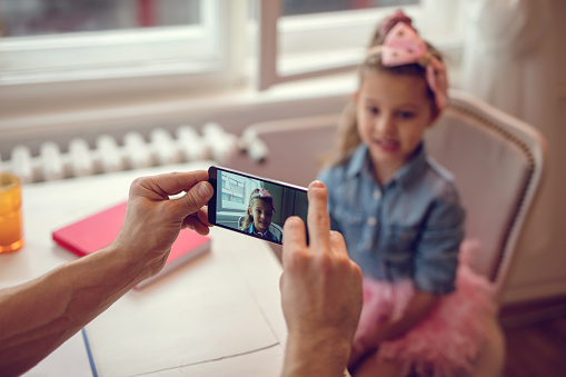 Close-up of father taking picture of his daughter with smart phone at home.