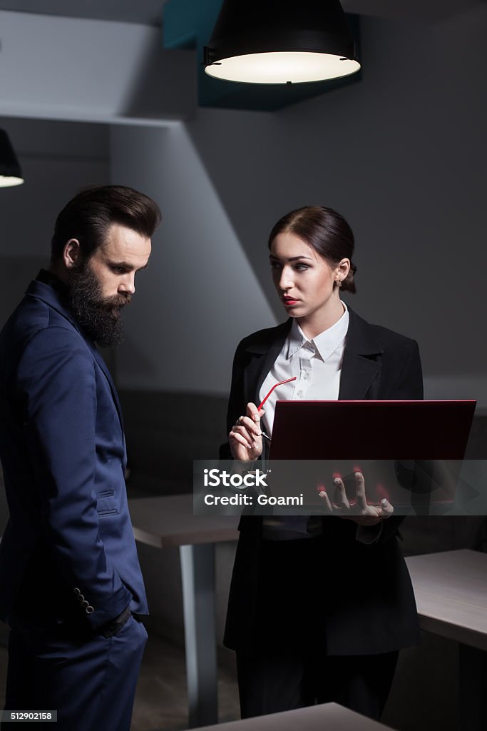 teamwork and business meeting of successful corporate office wor businessman and businesswoman dressed in suits and with laptop; male and female; girl with red lips and glasses and bearded guy; Adult Stock Photo