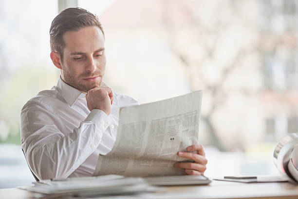 istock Handsome young businessman reading newspaper at office desk 512904084