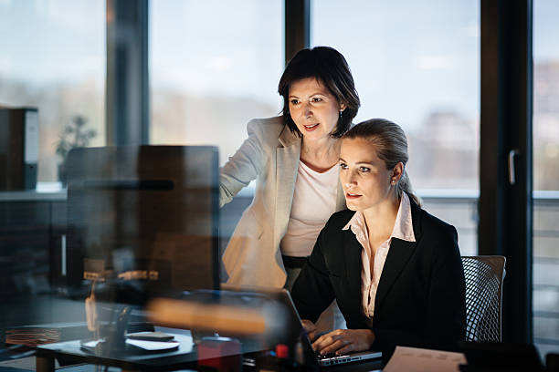 młody i dojrzały biznes kobieta pracuje się późno - computer computer monitor women business person zdjęcia i obrazy z banku zdjęć