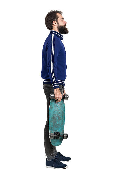 istock Side view of young hipster in tracksuit jacket carrying skateboard 512906564