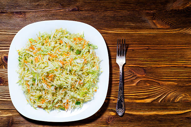 Fresh vegetable salad with cabbage, carrots, green onions and dill on a wooden background.