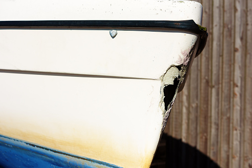 A damaged sailboat resting outside a building. A large hole is in the fore of the keel. Close up of the hole.