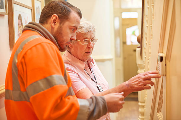 heating system for senior woman a heating engineer demonstrates to a senior woman in her home how to set the thermostat.  heating engineer stock pictures, royalty-free photos & images