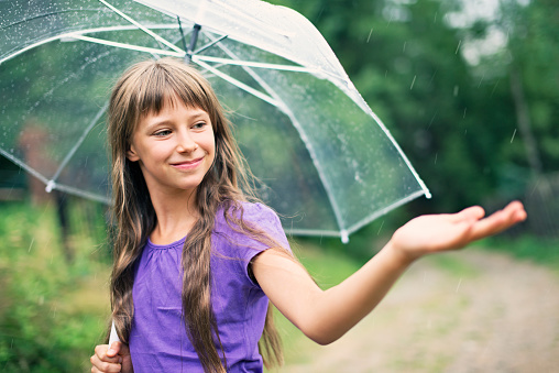 Little girl enjoying spring or summer rain. The girl aged 9 is holding the umbrella and checking the rain with smile.
