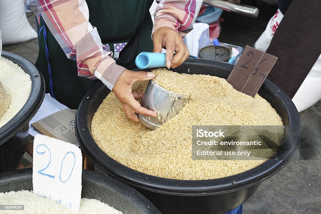 Selling Thai rice. Chiang Dao, Thailand - September 16, 2014: A rice seller filling a container whilst selling brown Thai Jasmine rice in the weekly Tuesday morning market.  Market Vendor Stock Photo