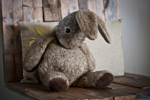 A photograph of an old toy rabbit sitting on a wooden chair.