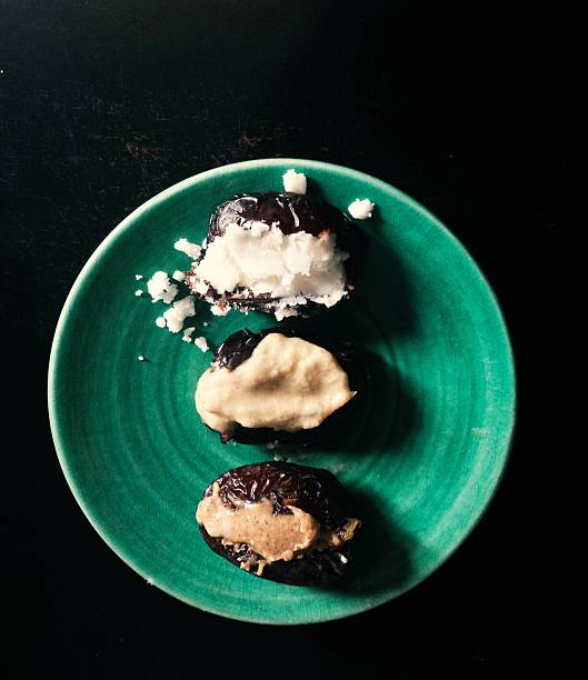 Three medjool dates on a green plate, each stuffed with one of coconut butter, sesame tahini or peanut butter. Shot top down on a dark background with copy space.