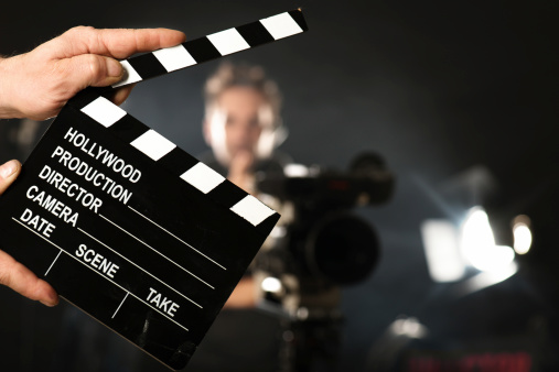 Senior movie director holding a movie clapper over isolated gray background, studio shot. Image taken with Hasselblad H5D 50C camera system and developed from camera RAW.