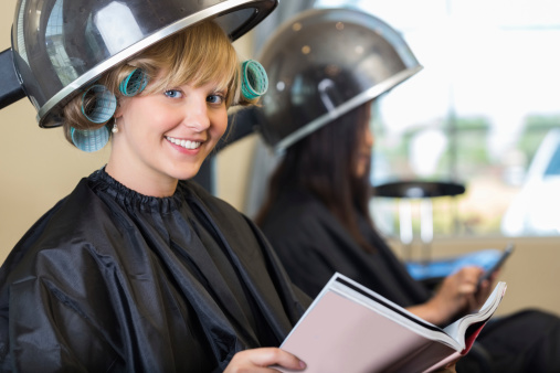 Salon customer reading magazine while hair dries in rollers