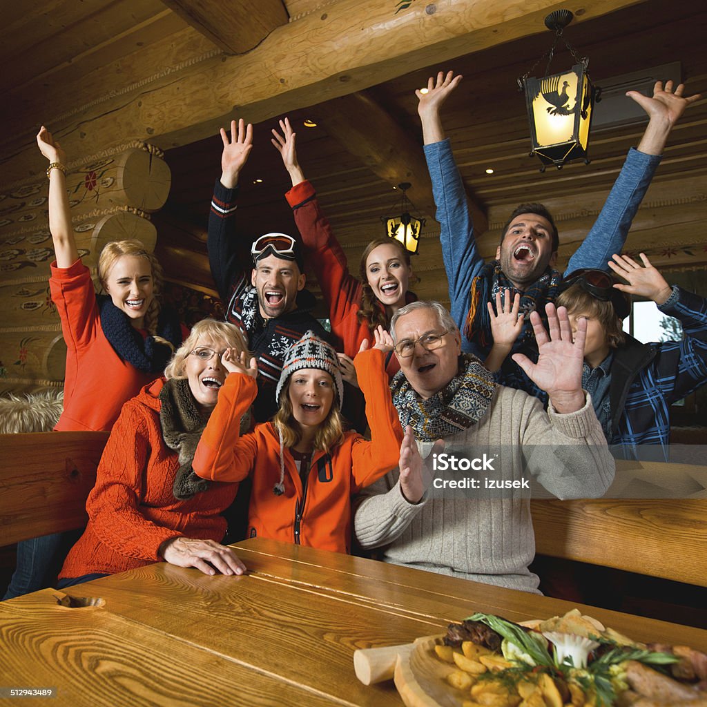 Group of people in mountain restaurant An excited multi-generation family sitting in a mountain restaurant after skiing and laughing with raised hands. Family Stock Photo