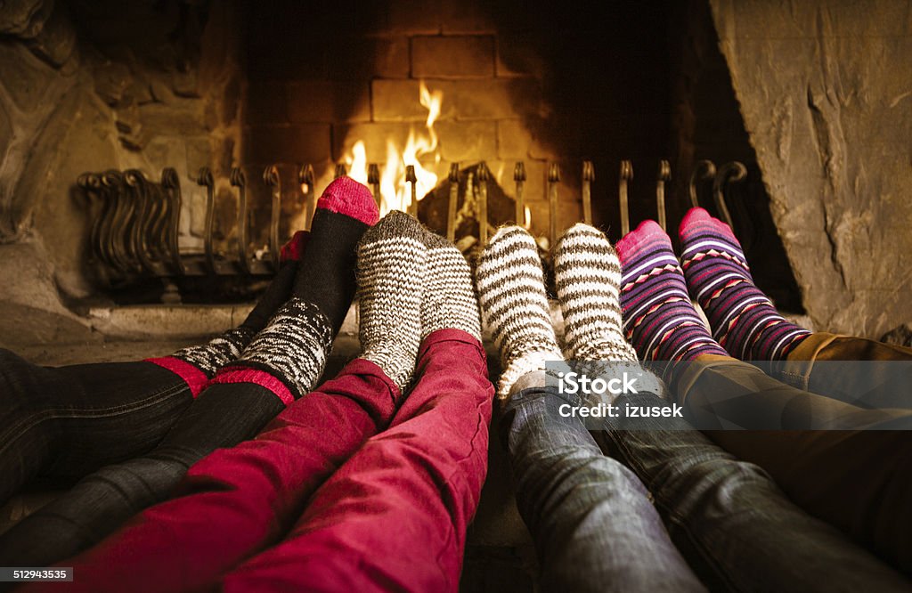 Friends sitting by the fireplace Four people warming their feet by the fireplace. Winter Stock Photo