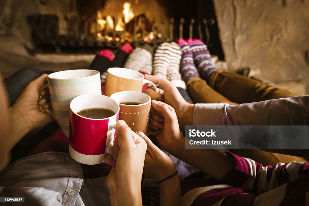 Friends sitting by the fireplace Four people warming their feet by the fireplace and drinking hot chocolate. Fireplace Stock Photo