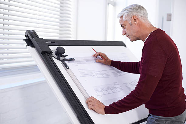 Doing what he does best Cropped shot of a male architect working on a building plan at a drawing board drawing board stock pictures, royalty-free photos & images