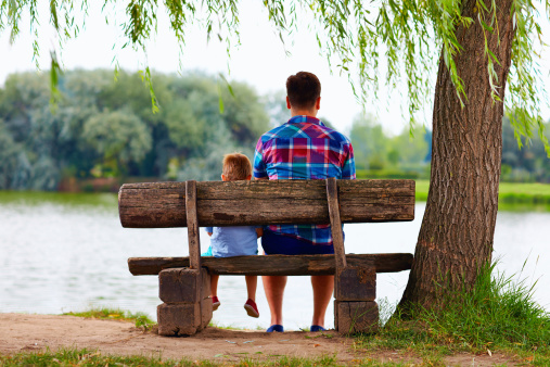 father and son sitting on the bench near the lake