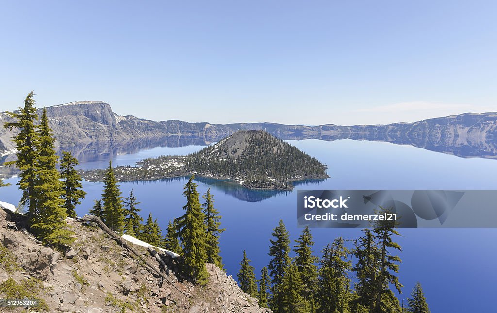 Crater Lake National Park, Oregon Clear blue water of Crater Lake National Park in Oregon during early spring with some snow left from winter. Wizard Island in the distance. At The Edge Of Stock Photo
