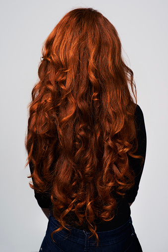 Studio shot of a young woman with beautiful red hair posing against a gray background