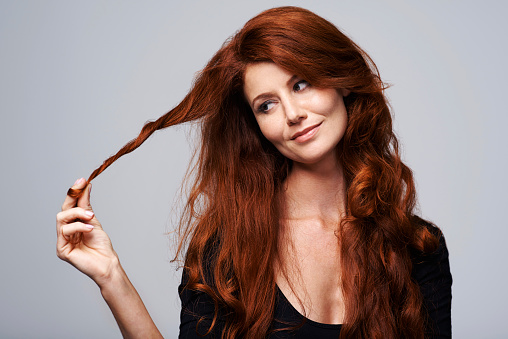 Studio shot of a young woman holding her beautiful red hair against a gray background