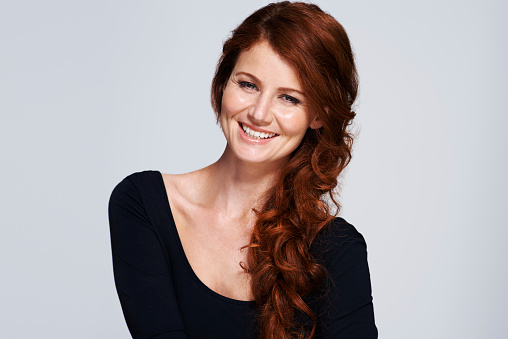 Studio shot of a young woman with beautiful red hair posing against a gray background