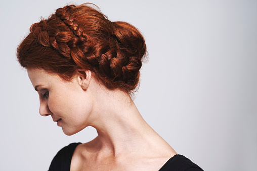 Studio shot of a beautiful redhead woman with a braided up-do posing against a gray background