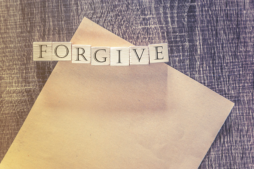 Forgiveness concept. Wooden blocks forming Forgive word on top of a blank paper. Cross processed image for vintage feeling