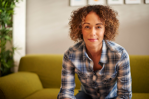 a woman sits on a sofa and looks confidently to camera with an assured smile .