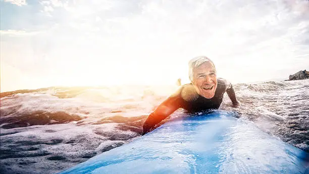Active and happy senior man living to the fullest, surfing on a surfboard during his summer vacation 