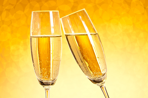 Two glasses of champagne toasting against gold bokeh background