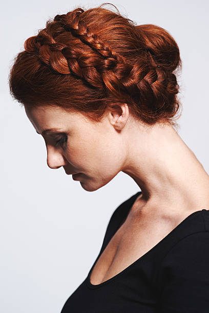 Beautifully braided Studio shot of a beautiful redhead woman with a braided up-do posing against a gray background braided buns stock pictures, royalty-free photos & images