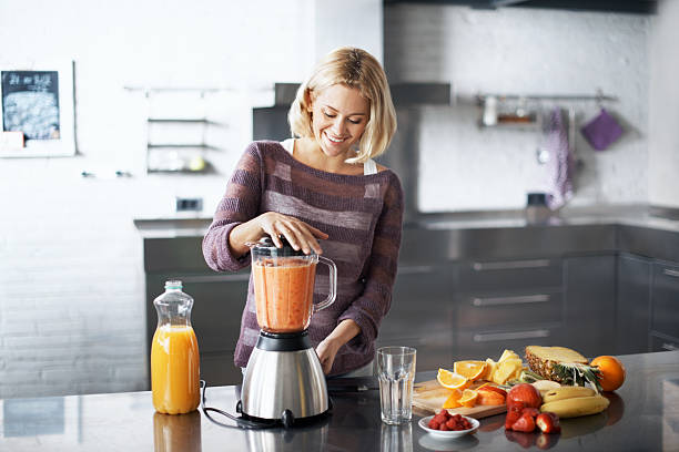 Impressed with her culinary skills A woman smiling happily while preparing a smoothie in her kitchen at home blender photos stock pictures, royalty-free photos & images