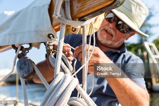 Man Secures Canvas On The Boom Of A Sailboat Stock Photo - Download Image Now - Sail, Senior Adult, Sailing