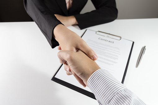 Businessman and businesswoman handshake over the  contact document.