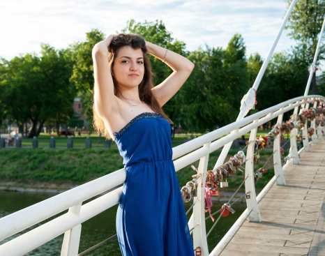 Beautiful young girl stands on bridge over the river