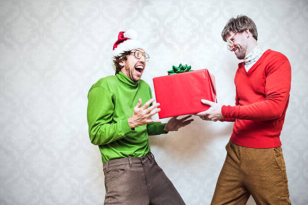Christmas Nerd Giving Present Two goofy looking men in ugly Christmas colored turtlenecks and sweaters exchange a holiday gift  Damask style vintage wall paper in the background.  Horizontal with copy space. christmas ugliness sweater nerd stock pictures, royalty-free photos & images