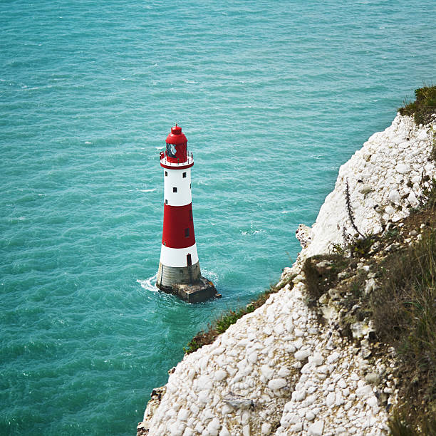 istock Red and white lighthouse closeup in cyan sea with cliffs 512987110