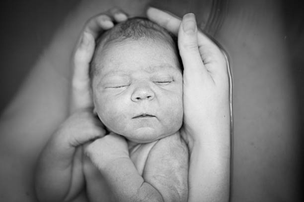 Mother Tenderly Holding Newborn After Home Water Birth Black and white image of a young mother holding her newborn son in the water after giving birth at home in a birthing tub. water birth stock pictures, royalty-free photos & images