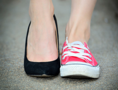 Two different shoes. On the street. Young adult or teen female standing still. Ankle shot.