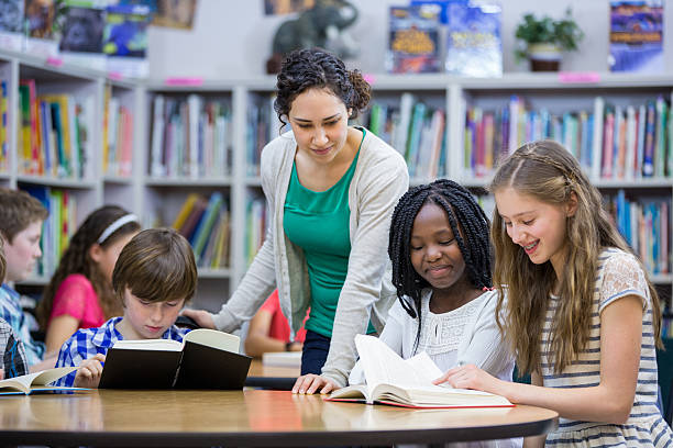 elementare schüler arbeiten mit lehrer in der bibliothek - kind im grundschulalter stock-fotos und bilder