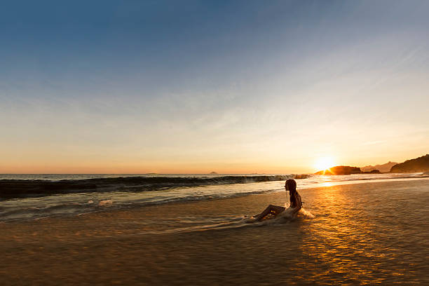 istock Little Girl Sitting on the Shallows on Empty Beach 512996274