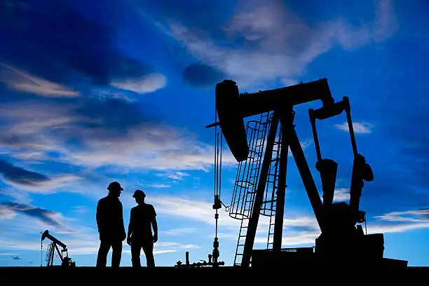 A royalty free image from the oil and gas industry of two oil workers in an oil field at dusk.