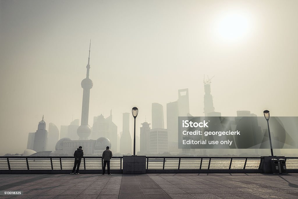 Shanghai Dawn Shanghai, China - March 5, 2013: Two men standing on the Bund side of the Hangpu River, silhouetted against the morning sun as it rises above the skyscrapers of Pudong. Air Pollution Stock Photo