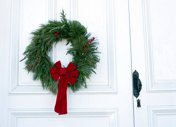 A Christmas Wreath of pine and a red bow graces a white church double door. 