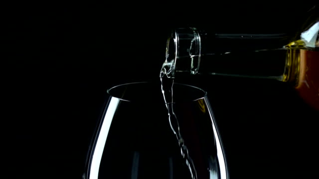 White wine being poured into a wineglass, black, slowmotion, closeup