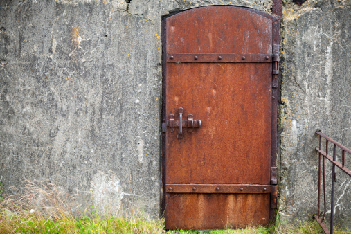Rusted metal door in old fortification wall, background texture