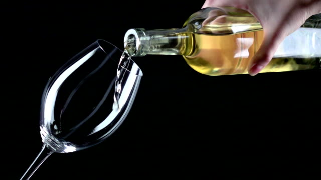 White wine being poured into a wineglass, black, closeup, slowmotion