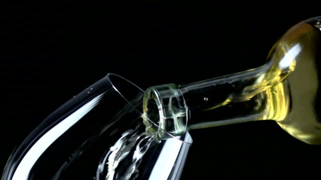 White wine poured into a wineglass, black, closeup, slowmotion