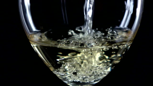 White wine is poured into a glass side view, black, closeup, slowmotion