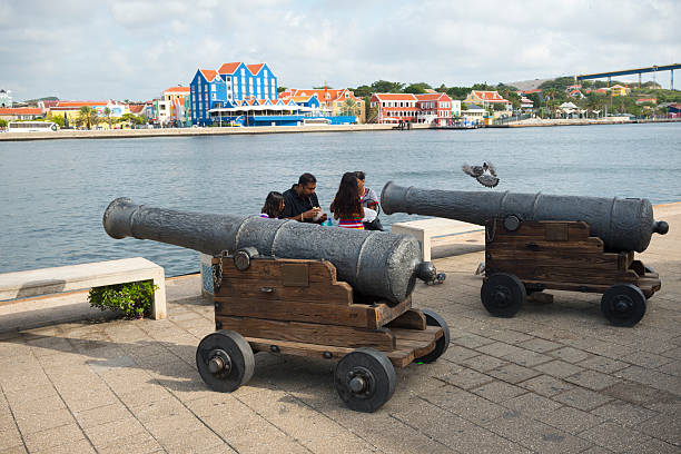 Family in Willemstad, Curacao Willemstad, Curacao - September 30, 2014: A family sits near two cannons in the Punda area of Willemstad, Curacao. The city centre has been designated a UNESCO World Heritage Site. pigeon family stock pictures, royalty-free photos & images