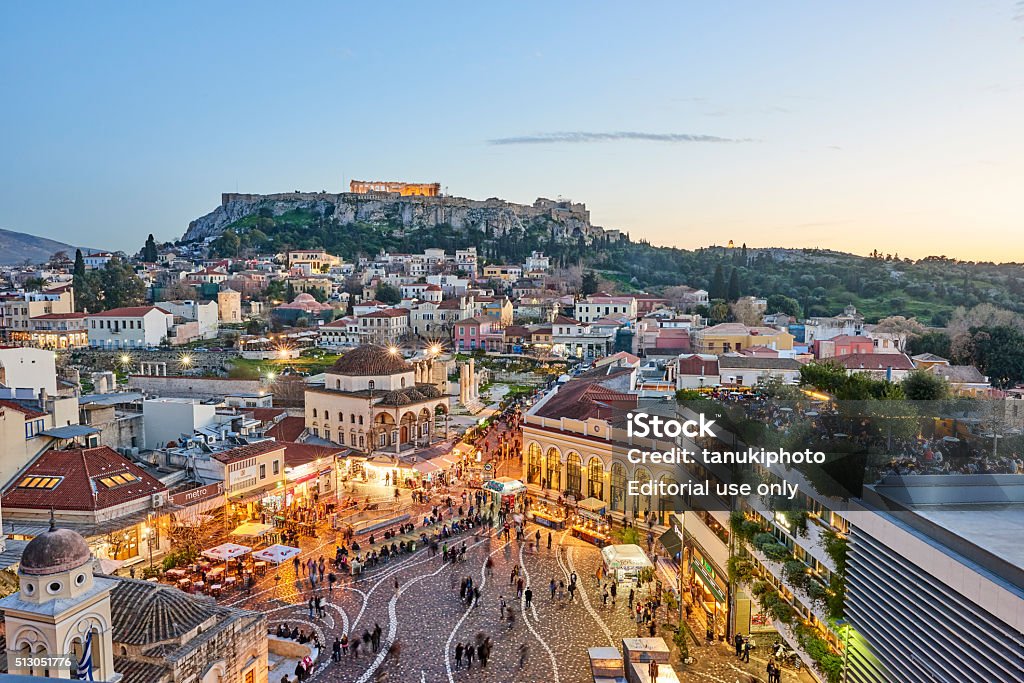 City of Athens and Acropolis by Evening Athens, Greece - February 13, 2016: Aerial view of Athens at sunset with an illuminated Acropolis in the background. In foreground tourists and local people in Monastiraki Square. The clustered homes on the hill is known as Plaka. Athens - Greece Stock Photo